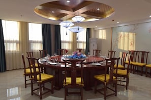 Une table de salle à manger ronde, entourée de chaises, un ventilateur de plafond et de grandes fenêtres avec des rideaux.