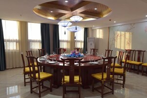 Una mesa de comedor redonda con sillas, un ventilador de techo y ventanas grandes con cortinas.