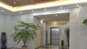 A lobby with a potted plant, a large vase, and a modern elevator. - Lan Tian Business Hotel (Wuyang)