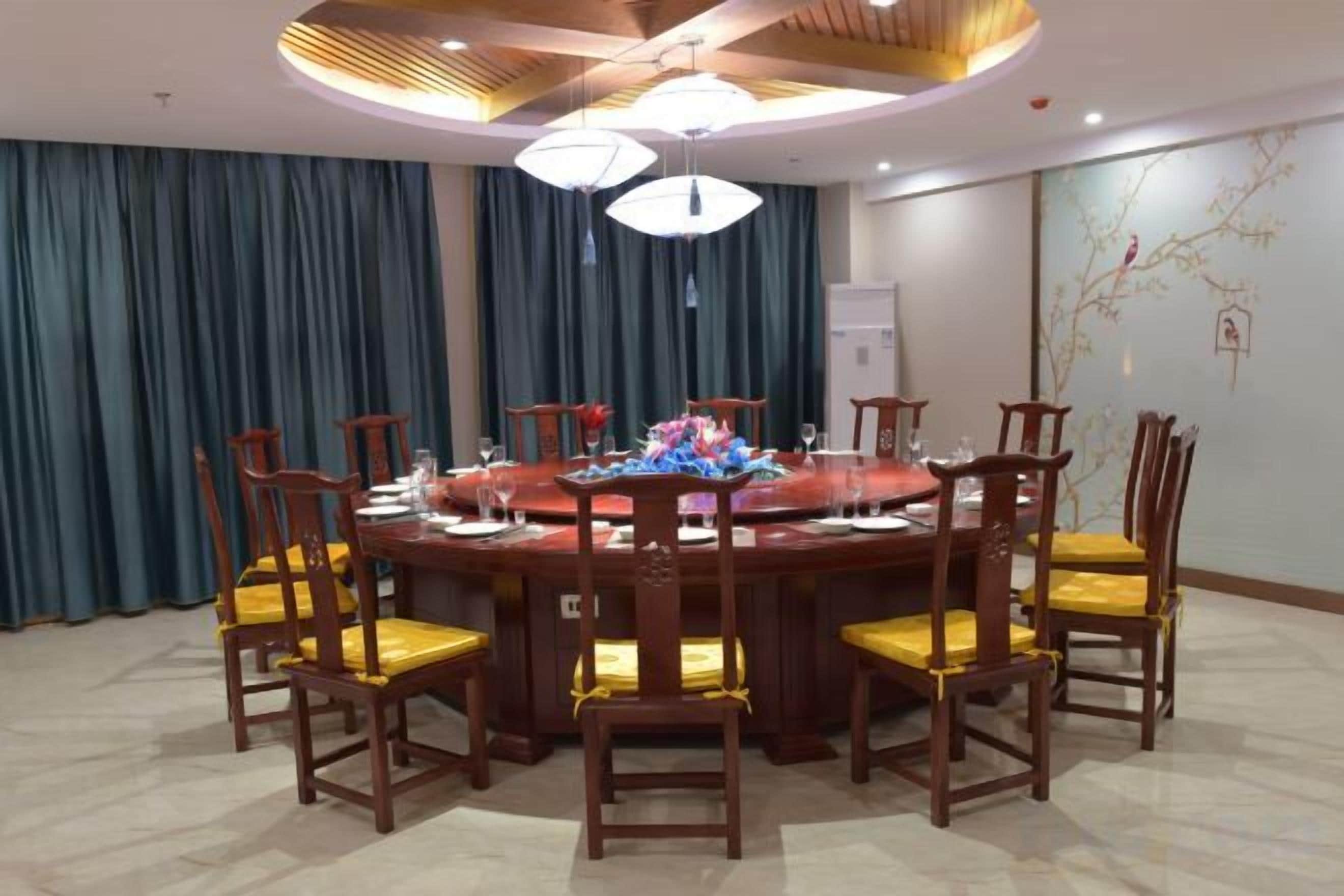 A round dining table with chairs, a chandelier, and a wall with a decorative branch.