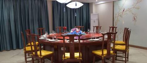 A round dining table with chairs, a chandelier, and a wall with a decorative branch.