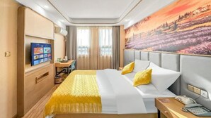 A hotel room with a bed, a desk, a chair, a TV, and a painting on the wall. - Lan Tian Business Hotel (Wuyang)