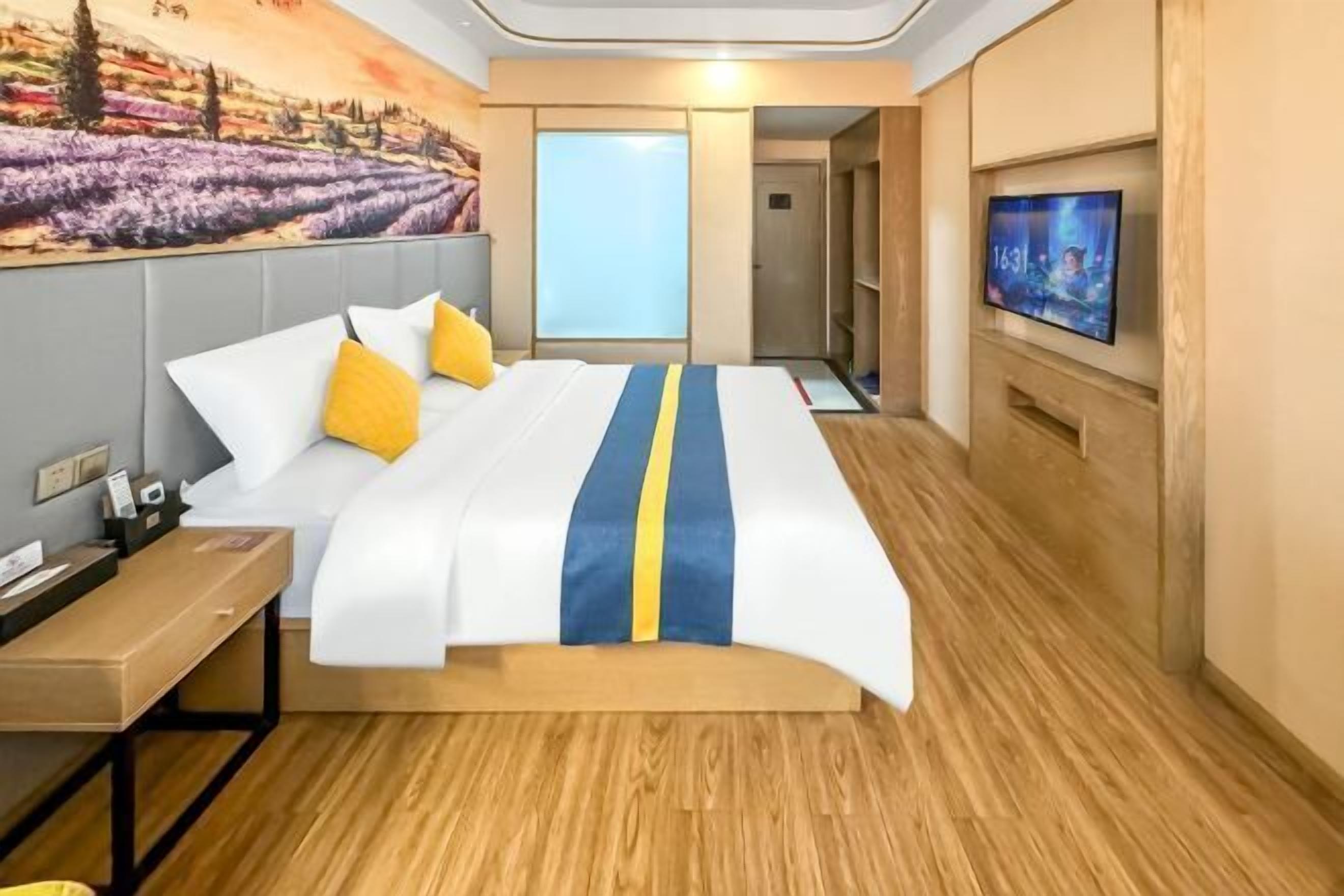 Habitación de hotel con cama, escritorio, televisor y un cuadro en la pared.