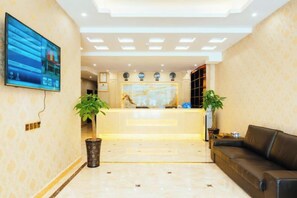 A hotel lobby with a reception desk, a television mounted on the wall, and a seating area with a sofa. - Bojuejioudian (Daozhen)