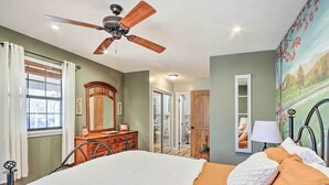 Une chambre à coucher avec un lit, un ventilateur de plafond, une commode, un miroir et un tableau accroché au mur.