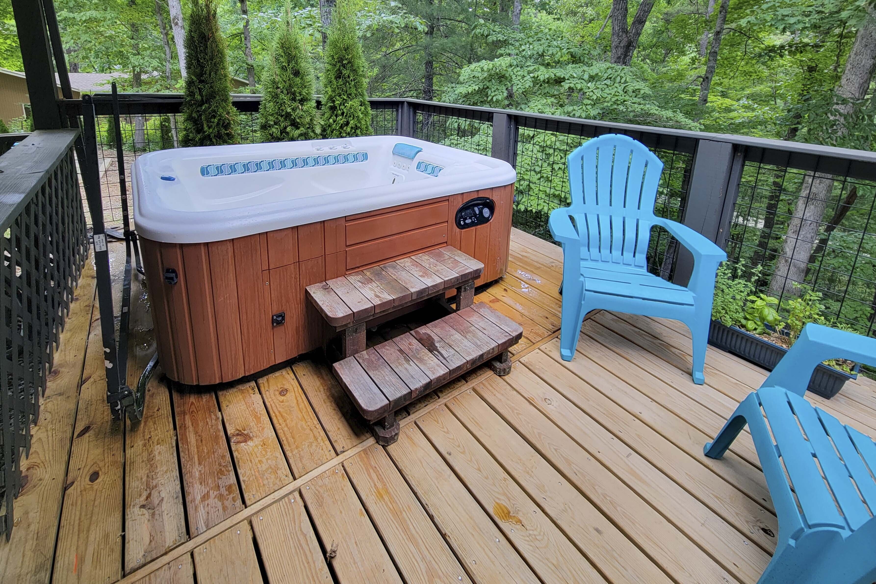 A wooden deck with a hot tub, wooden steps, and blue Adirondack chairs.
