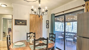 Un coin repas avec une table en bois, des chaises, un lustre et une vue sur la terrasse, visible à travers des portes vitrées.