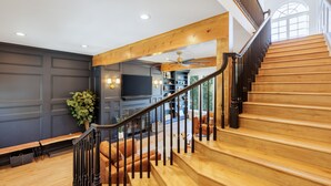 Una escalera de madera con barandilla oscura que conduce a una sala de estar con chimenea, sofás y televisor.