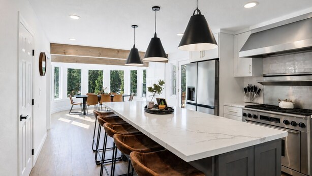 Una cocina moderna con una isla grande, electrodomésticos de acero inoxidable, iluminación colgante y vistas al exterior.
