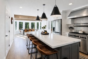A modern kitchen with a large island, stainless steel appliances, pendant lighting, and a view of the outdoors. - Moonridge Mansion Retreat • Sleeps 16+ • Spa • Sauna • Game Room • 5BR (Big Bear Lake)