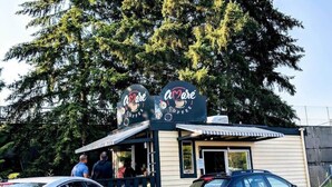 Una pequeña cafetería con un letrero que dice "Amore Coffee". Hay dos coches estacionados adelante y una persona visible en la entrada.