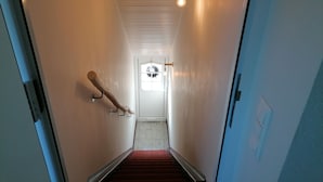 A narrow hallway with a wooden handrail, a light bulb hanging from the ceiling, and a door at the end. - Apartment (Castrop-Rauxel)