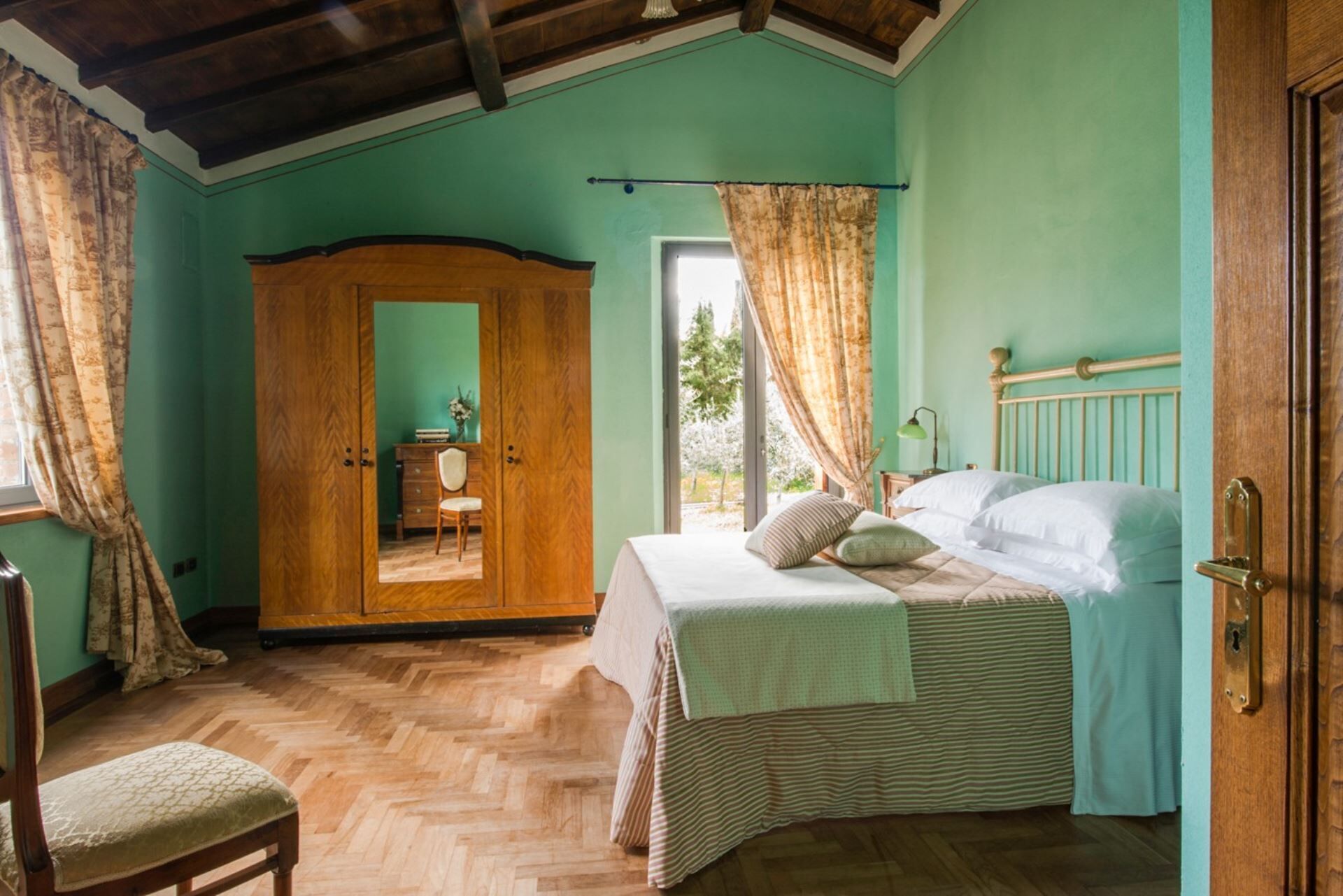 A bedroom with a bed, a wooden wardrobe, a chair, and a window with curtains.