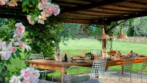 An outdoor dining area with a wooden table, wicker chairs, and hanging pendant lights. - Wonderful Villa in the heart of Chianti (Greve in Chianti)
