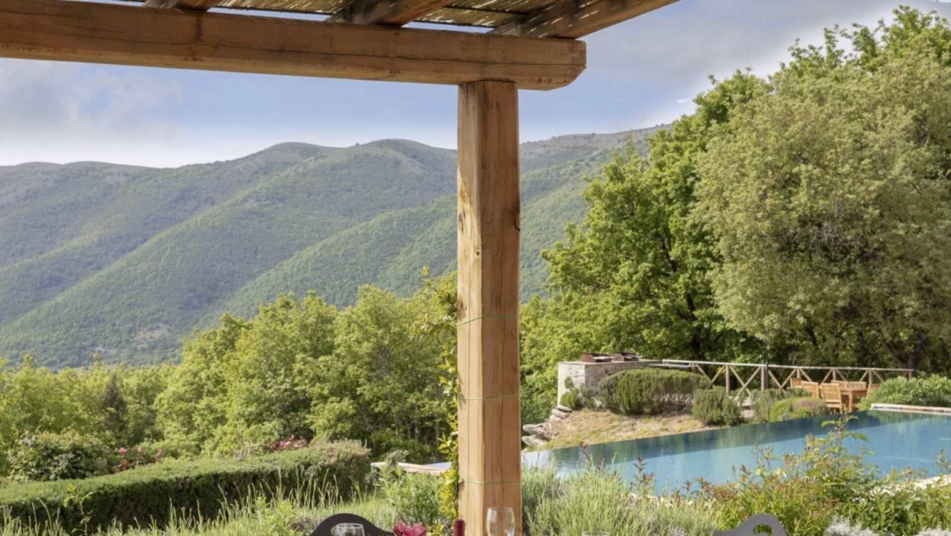 A pool with a mountain backdrop, wooden pergola, and lush greenery.