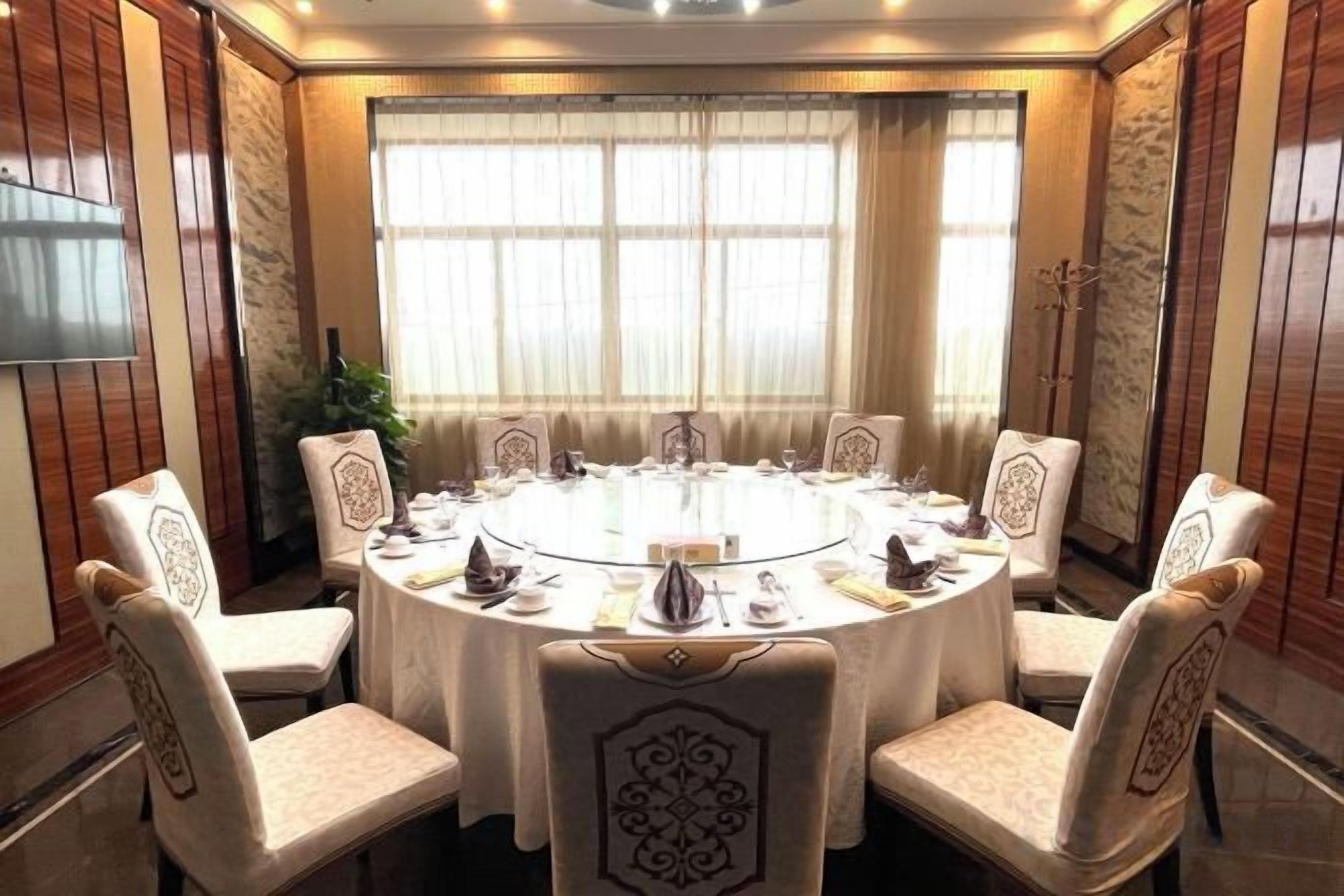A round table with eight chairs, each with a decorative backrest, in a room with large windows and curtains.