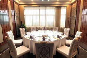 A round table with eight chairs, each with a decorative backrest, in a room with large windows and curtains. - Xikelai Hotel (Qingdao)