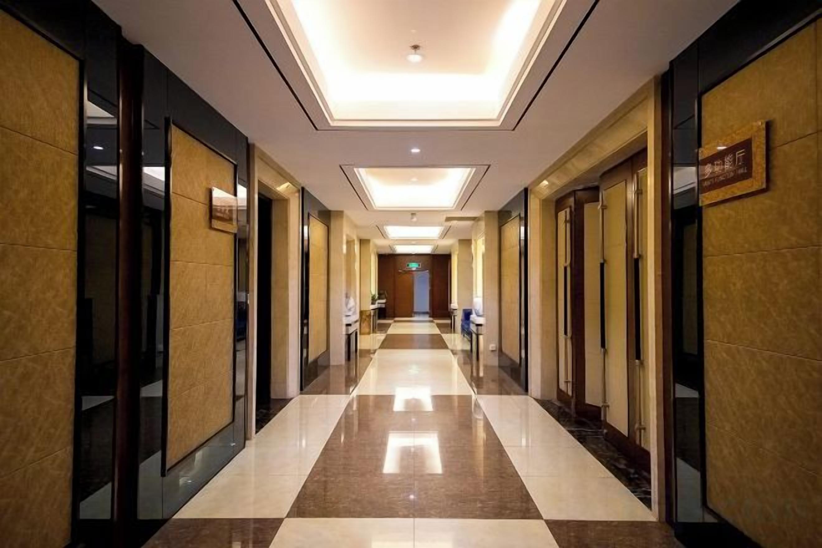 Pasillo de hotel con piso reflectante, puertas a ambos lados y un cartel en la pared derecha.