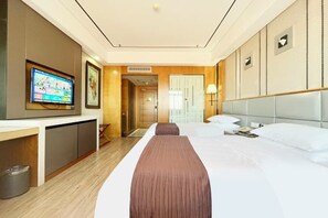 A hotel room with a large bed, a TV mounted on the wall, a desk, and a trash bin. - Xikelai Hotel (Qingdao)