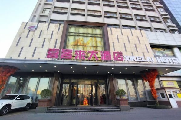 A hotel entrance with a modern facade, large windows, and a prominent sign. - Xikelai Hotel (Qingdao)