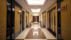 A hotel corridor with a checkered floor pattern, recessed ceiling lights, and mirrored walls. - Xikelai Hotel (Qingdao)