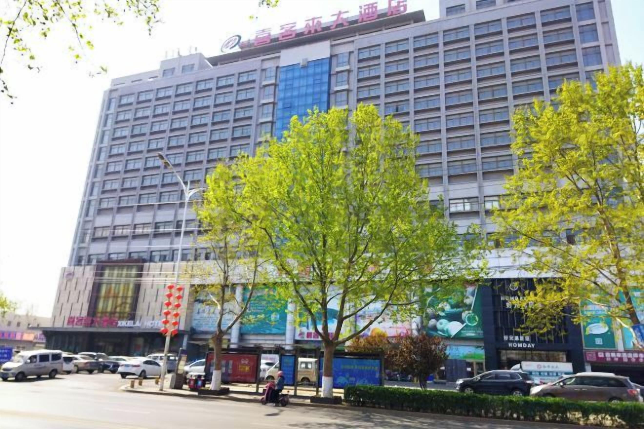 Un hotel de varios pisos con fachada moderna, un estacionamiento y algunos árboles en frente.