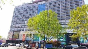 Un hotel de varios pisos con fachada moderna, un estacionamiento y algunos árboles en frente.