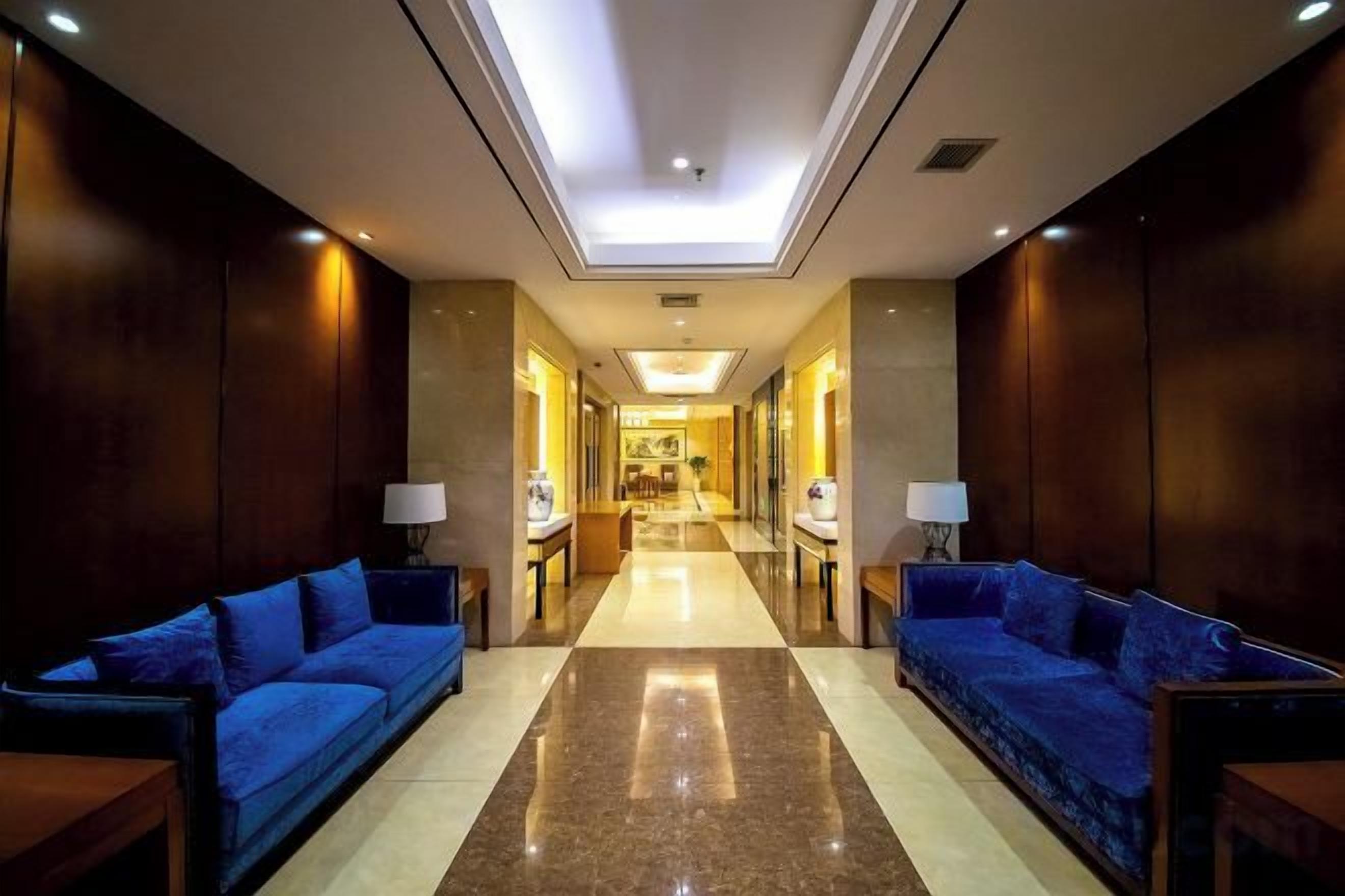 A hotel lobby with a central corridor, seating areas on either side, and a reception desk at the end.