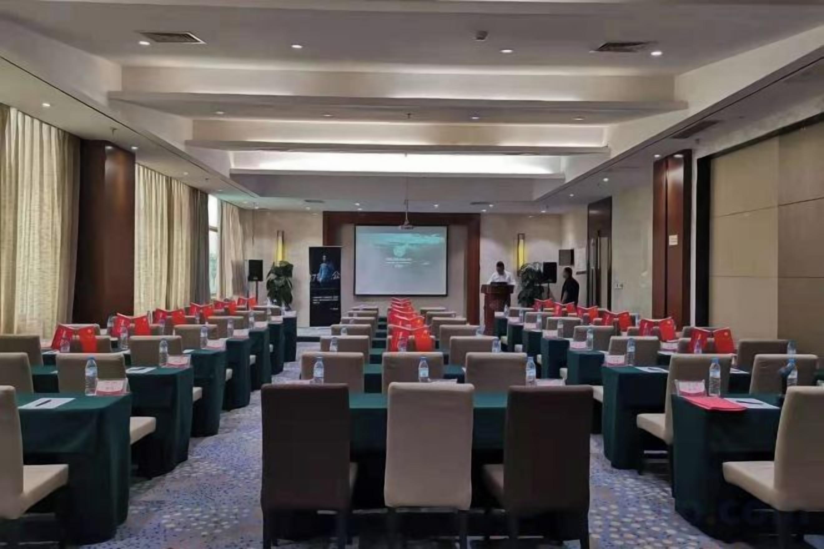 A conference room with rows of tables and chairs, a projector screen, and a speaker's podium.