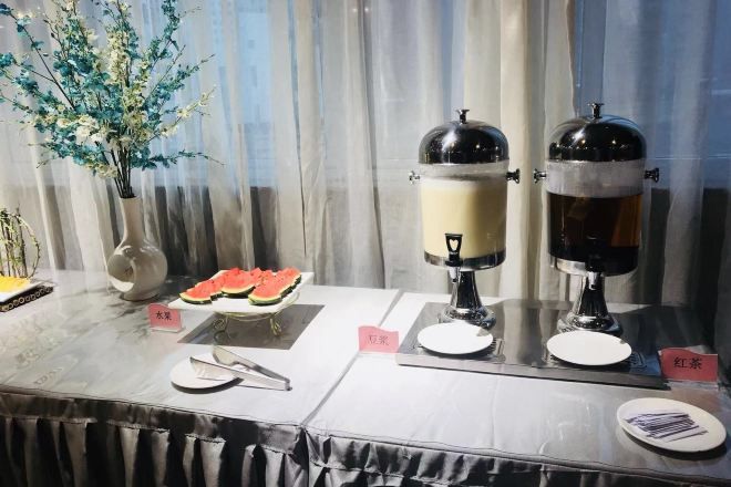 Ein Buffet mit zwei Kaffeeautomaten, einer Wassermelone und einer Vase mit künstlichen Blumen.