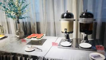 Ein Buffet mit zwei Kaffeeautomaten, einer Wassermelone und einer Vase mit künstlichen Blumen.