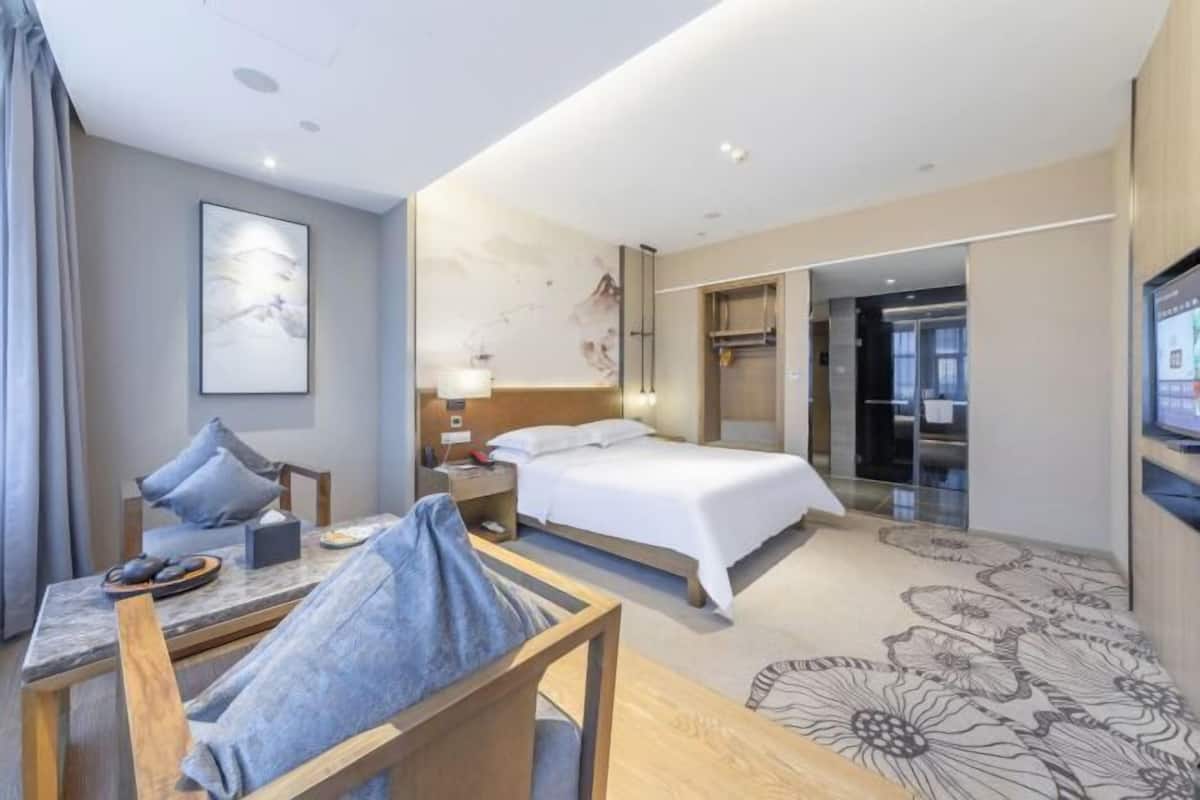 Ein Hotelzimmer mit Bett, Schreibtisch mit Stuhl, Fernseher und einem durchgegangenen Tür sichtbaren Badezimmer.