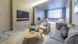 Une chambre d’hôtel moderne équipée d’un canapé, d’une table basse, d’un téléviseur fixé au mur et d’un lit donnant sur la ville.