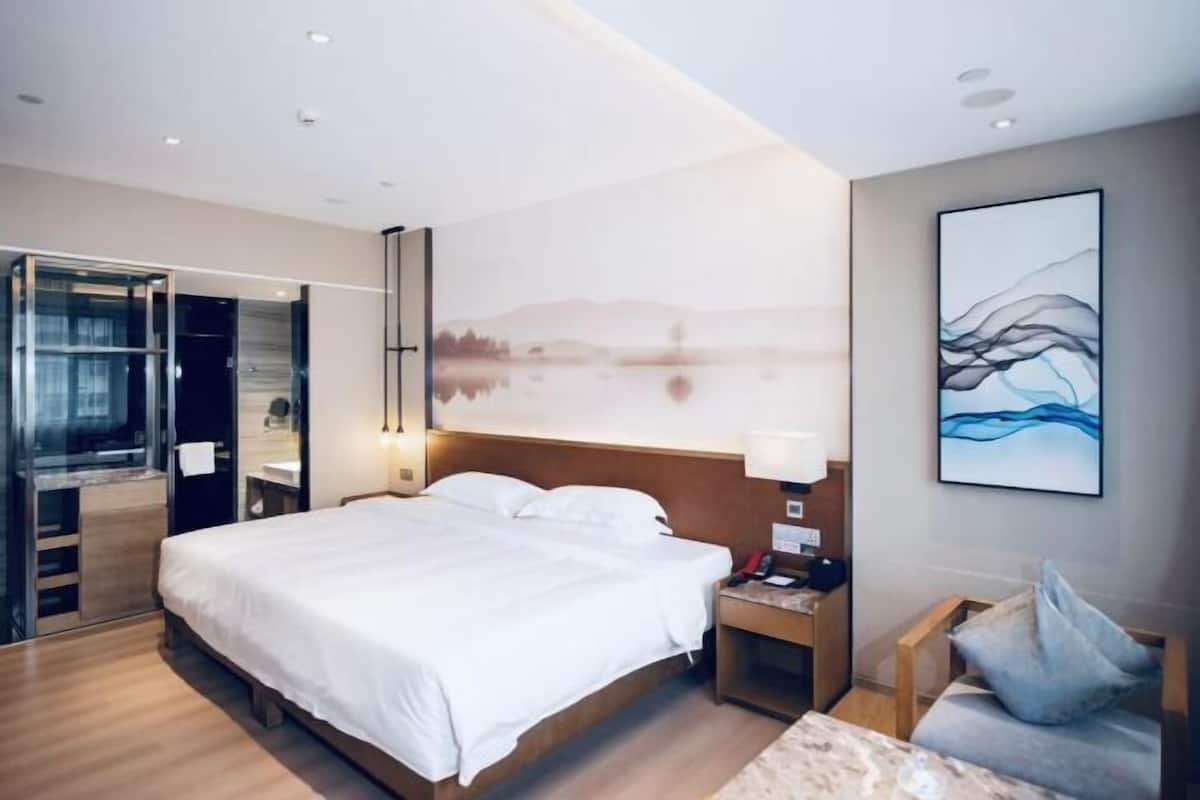 Ein modernes Hotelzimmer mit einem großen Bett, einem Nachttisch, einem Sessel und Seeblick durch ein großes Fenster.