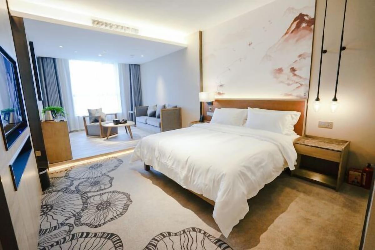 A hotel room with a large bed, a nightstand, a lamp, a wall-mounted TV, and a view of the room's interior.