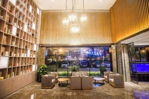A modern lobby with a marble floor, a seating area with sofas and tables, a bookshelf, and a view of the street through large windows. - Yijia Bauhinia Hotel (Yangjiang)
