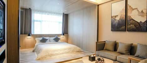 A modern hotel room with a bed, a sofa, a coffee table, and artwork on the wall.