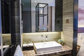 A modern bathroom with a large mirror, a rectangular sink, and a shower area. - Yijia Bauhinia Hotel (Yangjiang)