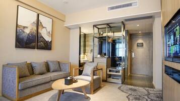 Una habitación de hotel moderna con sofá, sillón y mesa de centro. Hay un espejo grande y un televisor en la pared.