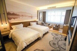 Habitación de hotel con dos camas, un sofá, un escritorio y un ventanal con cortinas.