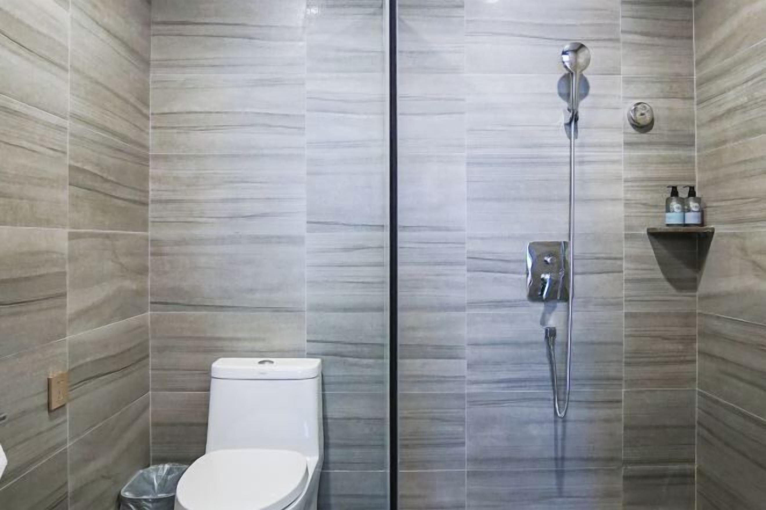 Une salle de bain moderne avec une douche à parois de verre, des toilettes et une petite étagère contenant des articles de toilette.