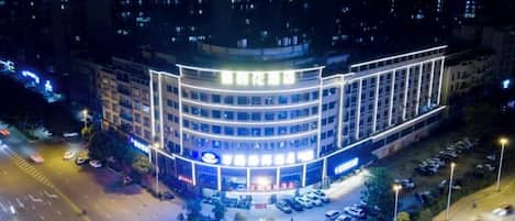 Un hôtel à plusieurs étages, doté d’une façade incurvée, de nombreux espaces de stationnement et d’une entrée bien éclairée.