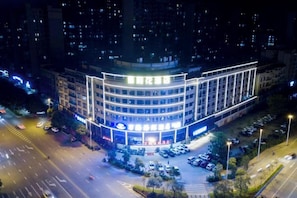 A multi-story hotel with a curved facade, multiple parking spaces, and a well-lit entrance.