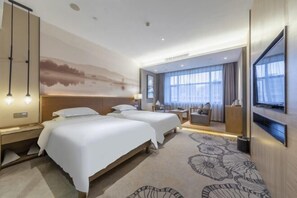 Hotelkamer met twee bedden, een bureau, een stoel, een televisie en een groot raam met gordijnen.