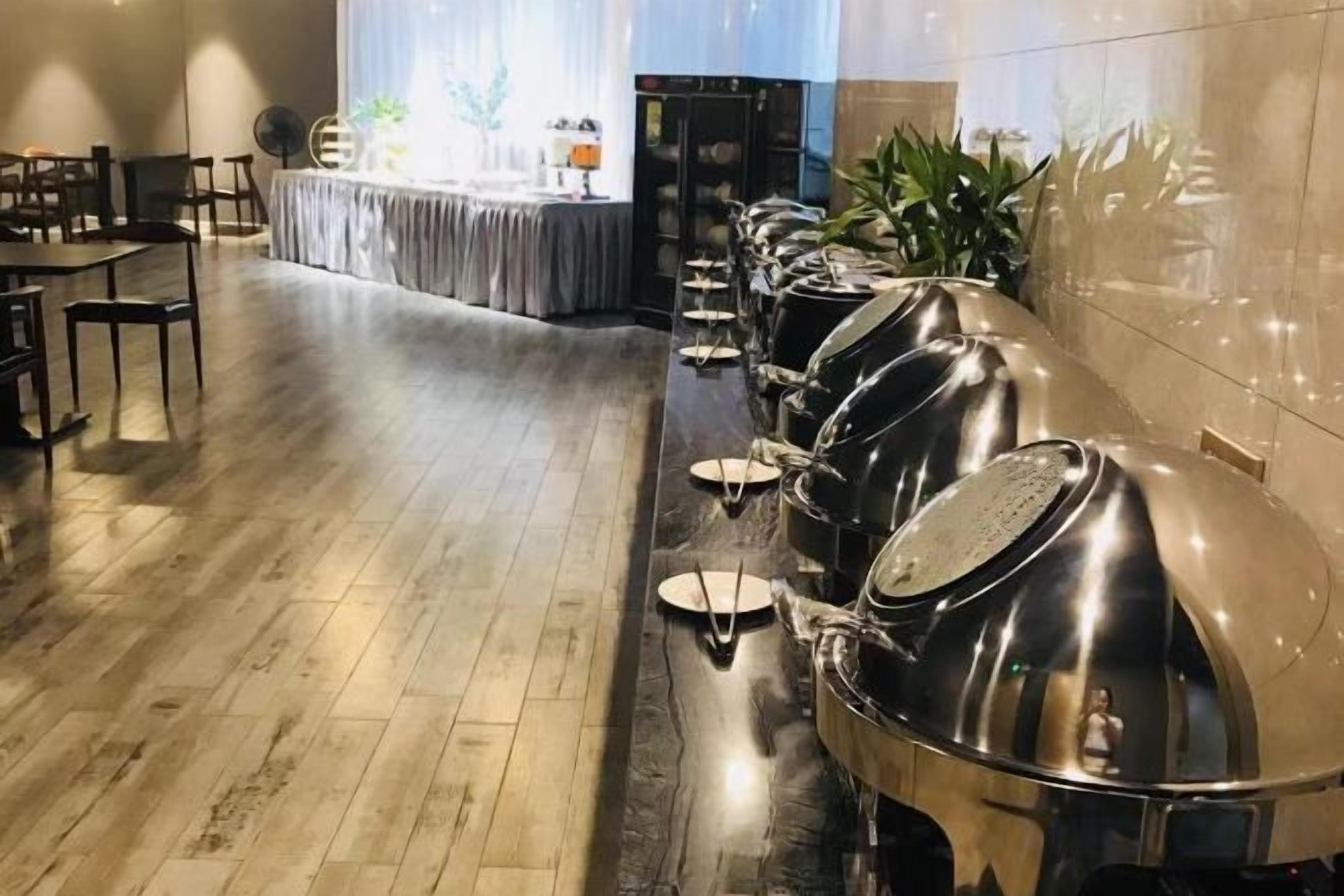 Una larga barra de buffet con estaciones de servicio de acero inoxidable y una mesa dispuesta para comer al fondo.