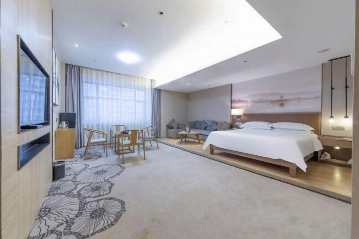 Ein modernes Hotelzimmer mit einem großen Bett, einem Schreibtisch und einem Stuhl. An der linken Wand befindet sich ein Fernseher, an der rechten Wand ein Gemälde.