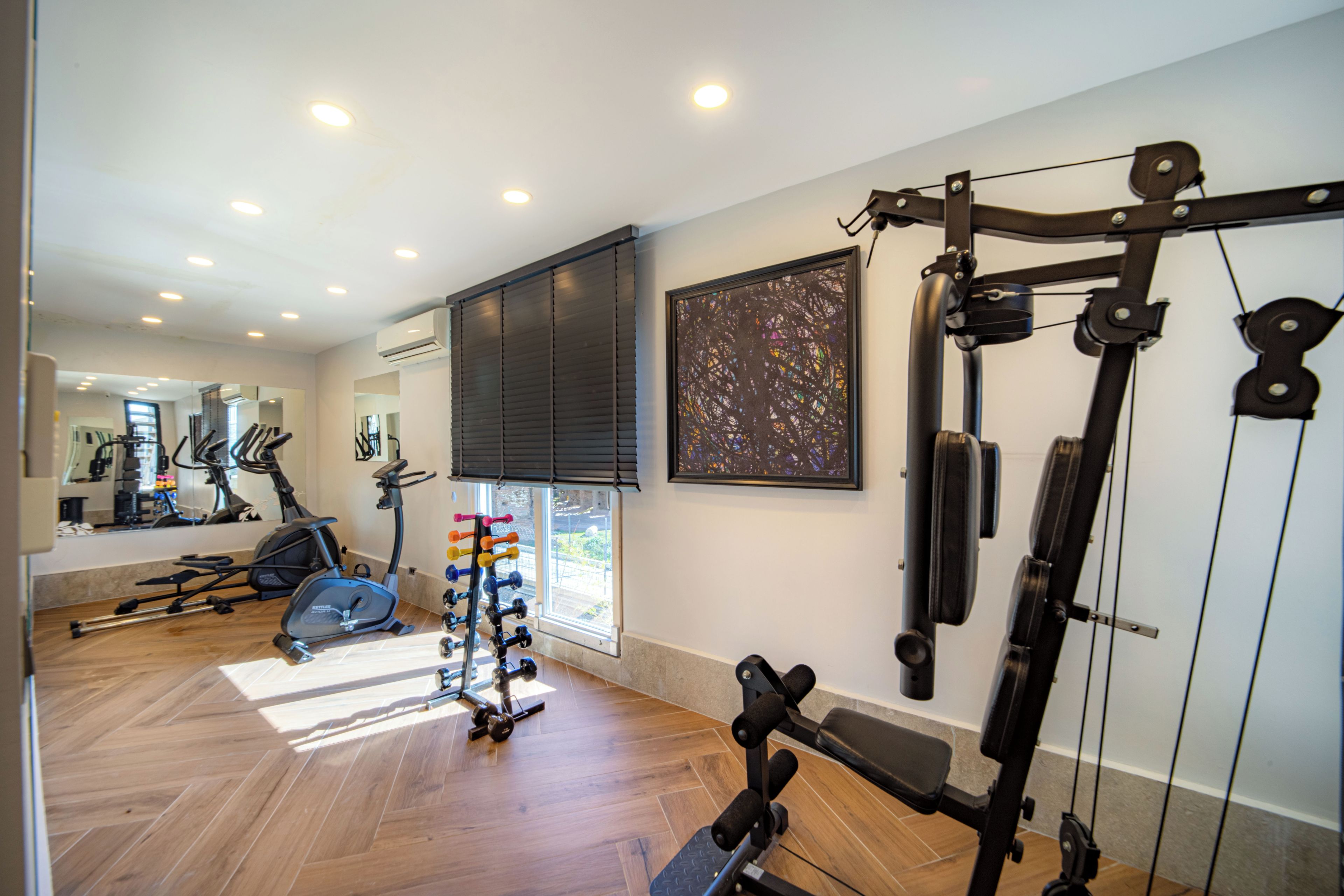 A gym with exercise equipment, a large mirror, and a window with blinds.