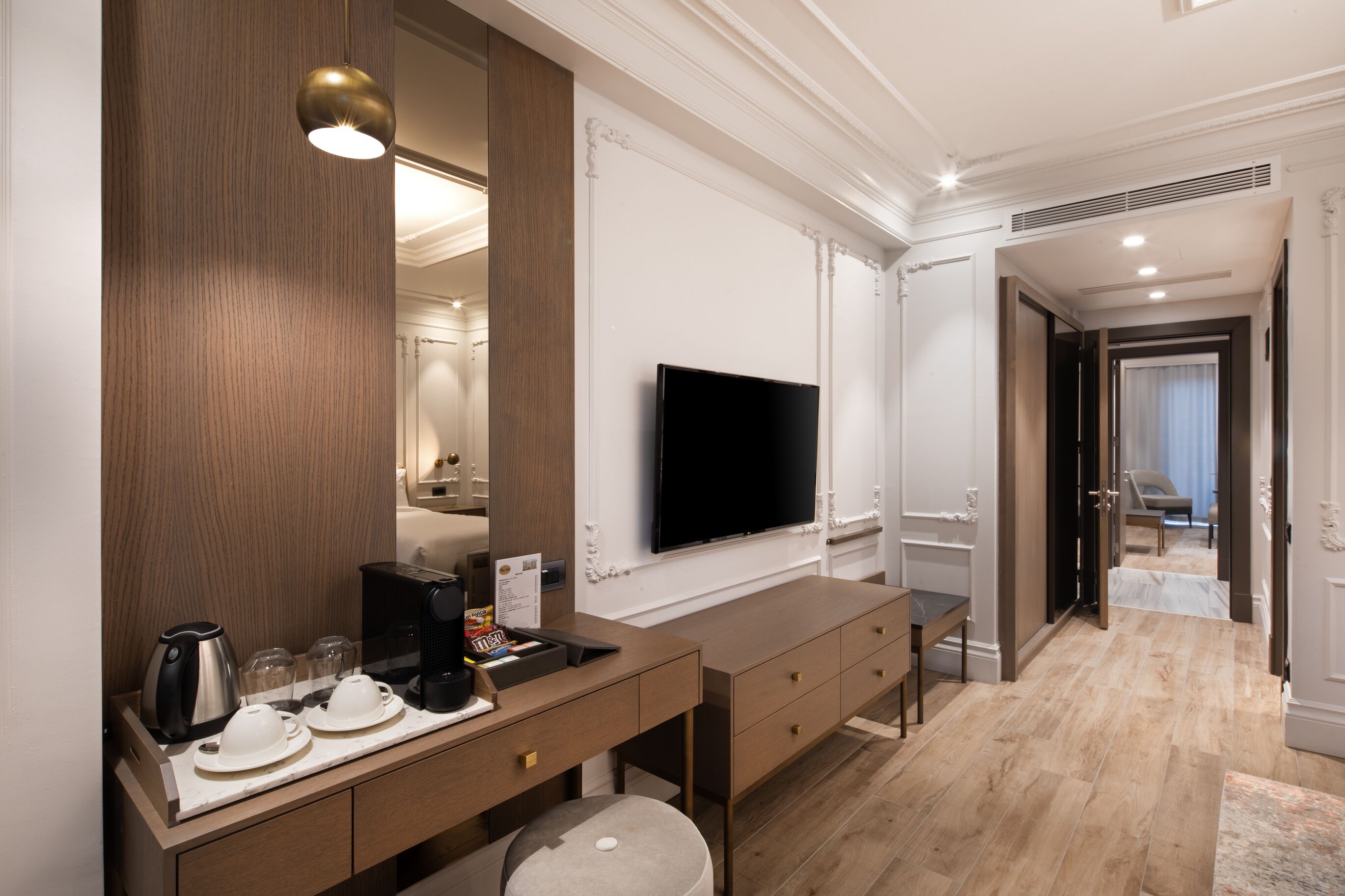 A hotel room with a wooden desk, a flat-screen TV, a coffee maker, and a mirror.