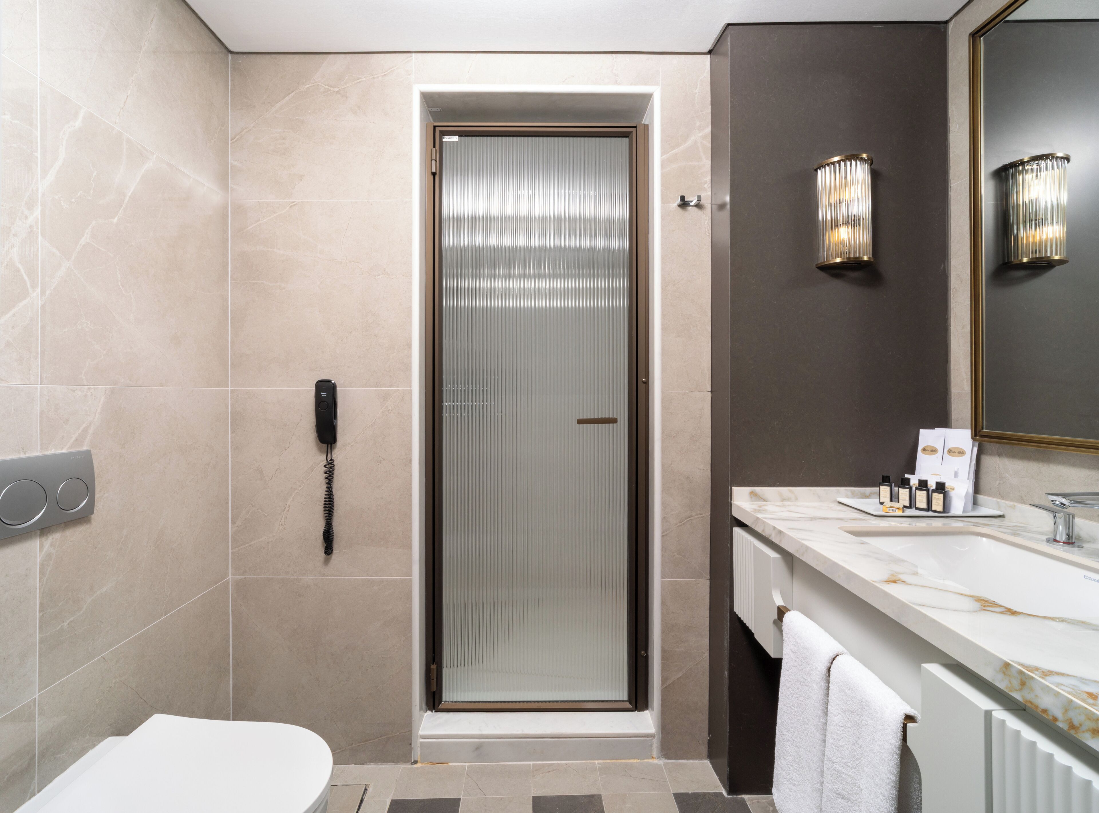 A modern bathroom with a glass-enclosed shower, a marble vanity, and a telephone on the wall.