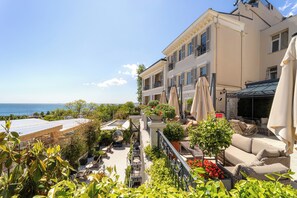 Eine Dachterrasse mit Sitzgelegenheiten im Freien, Kübelpflanzen und Meerblick.